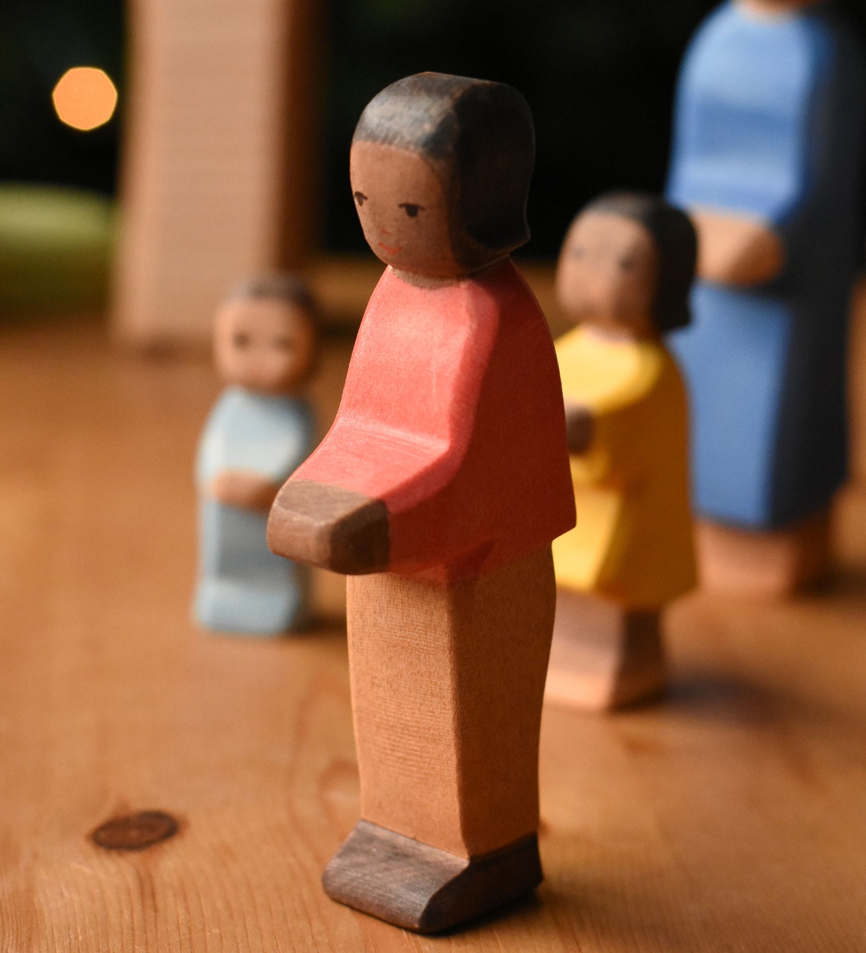 An Ostheimer son wooden toy figure with brown skin placed at the front of a small world play scene. These wooden figures are part of a wide range of expertly hand crafted wooden toys here at Babipur.