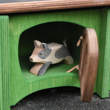 Ostheimer spotted piglet wooden toy animal figure placed in the green hutch with the brown door ajar. 