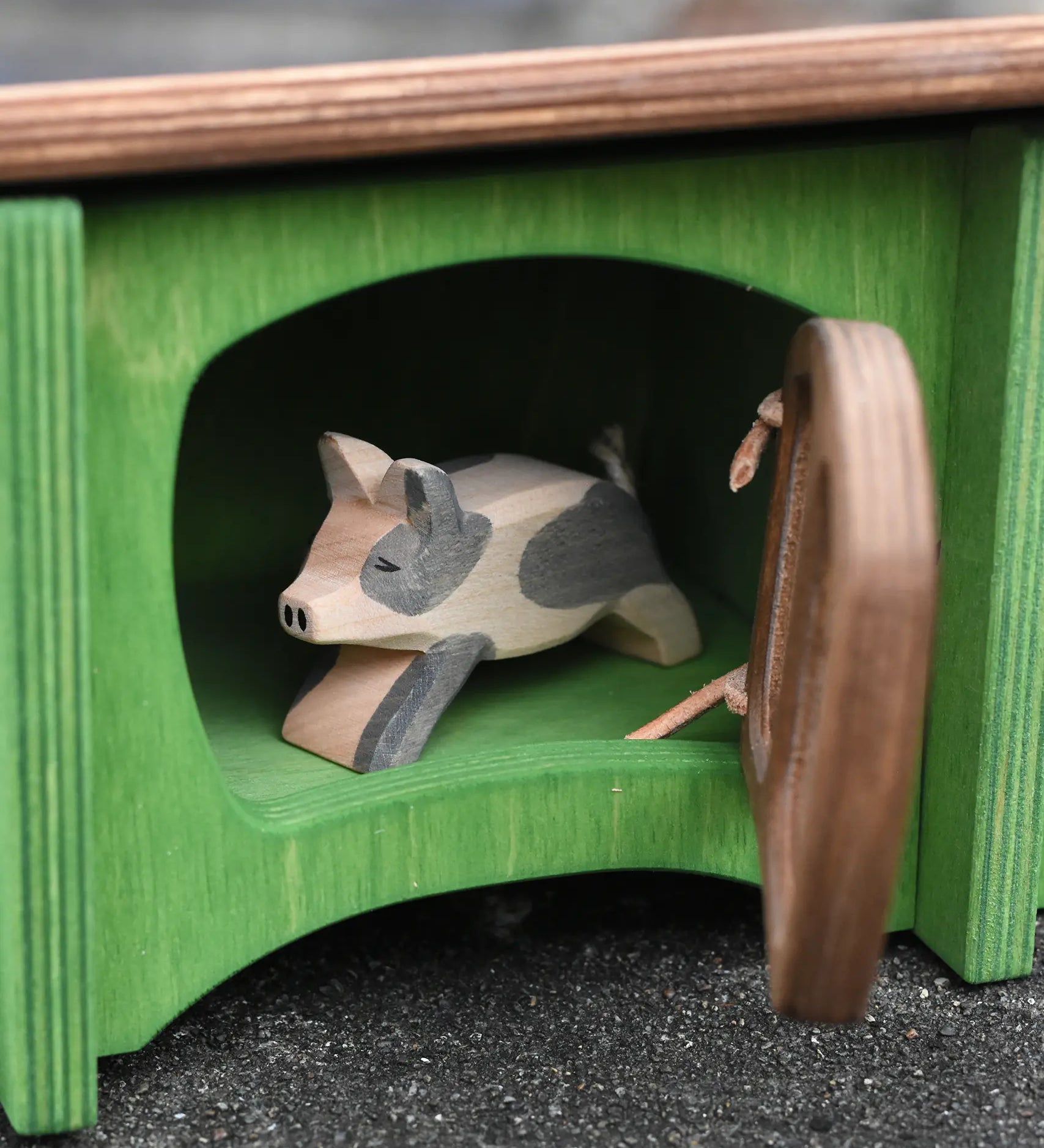 Ostheimer spotted piglet wooden toy animal figure placed in the green hutch with the brown door ajar. 