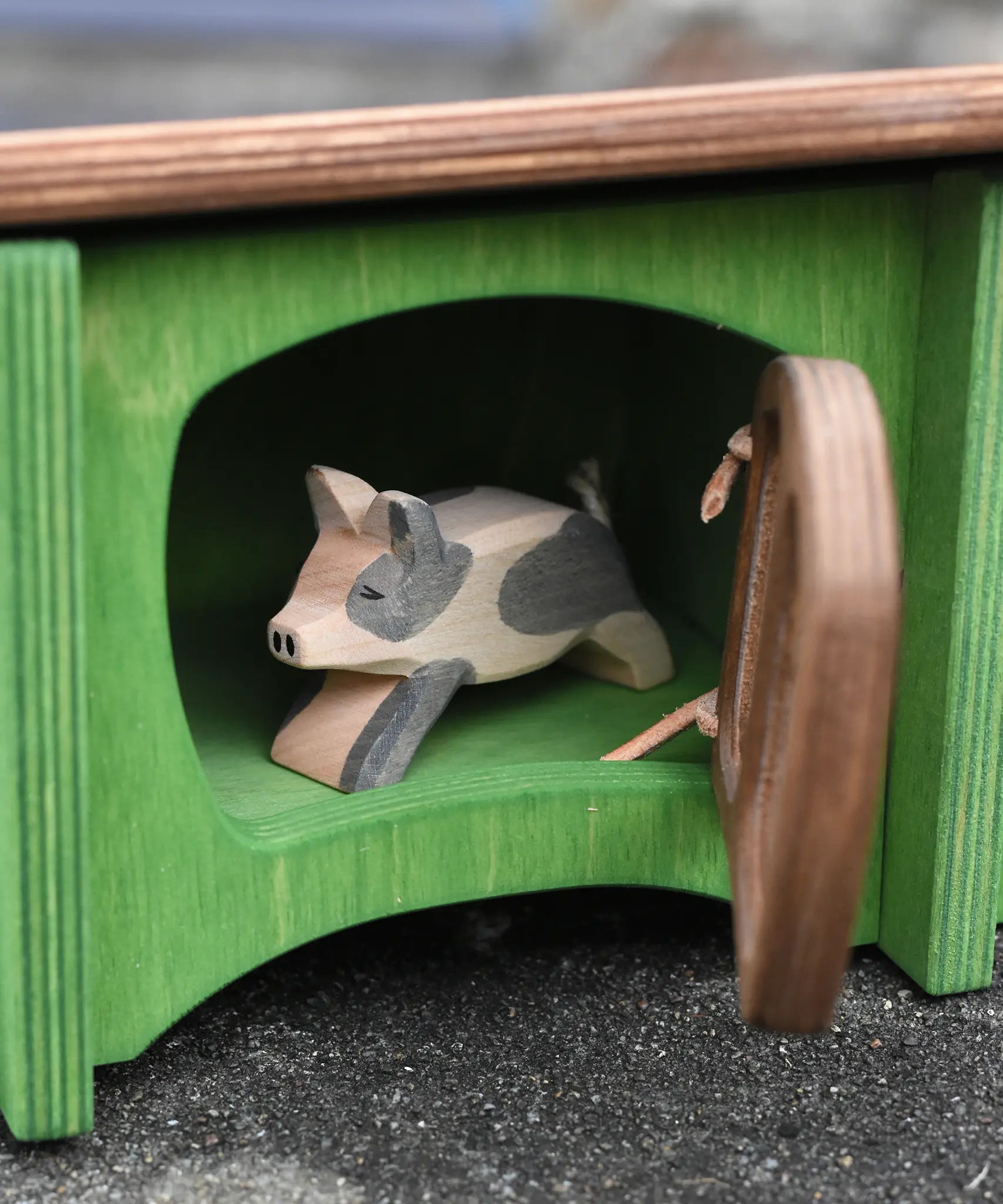 Ostheimer spotted piglet wooden toy animal figure placed in the green hutch with the brown door ajar. 