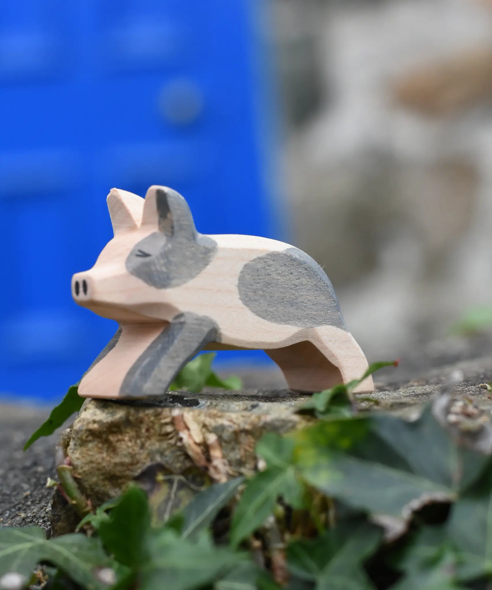 Ostheimer spotted piglet wooden toy animal figure placed on a stone wall outdoors