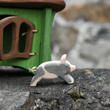Ostheimer spotted piglet wooden toy animal figure placed on a stone wall outdoors with a green hutch in the background.