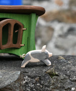 Ostheimer spotted piglet wooden toy animal figure placed on a stone wall outdoors with a green hutch in the background.