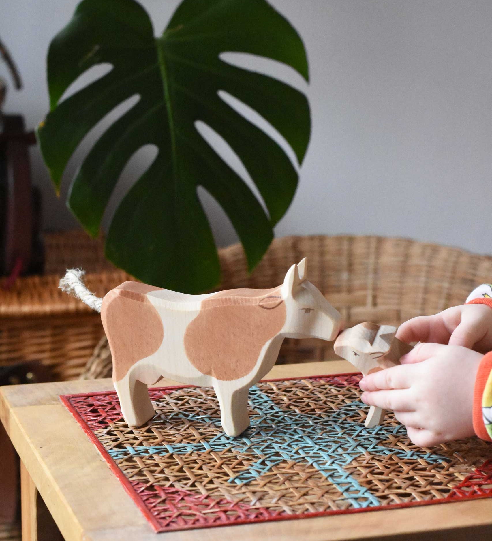 Child playing with Ostheimer brown standing cow figure placing a calf in front of it. 