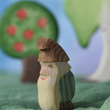 An Ostheimer standing fire tree dwarf wooden toy figure placed in a small world play scene. The dwarf figure has a green coloured outfit with brown hat and a long white beard. The figure has been placed on a green coloured Ostheimer play scarf. This wooden figure is part of a large range of expertly hand crafted, Waldorf inspired, wooden toys here at Babipur. 