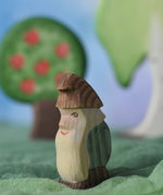 An Ostheimer standing fire tree dwarf wooden toy figure placed in a small world play scene. The dwarf figure has a green coloured outfit with brown hat and a long white beard. The figure has been placed on a green coloured Ostheimer play scarf. This wooden figure is part of a large range of expertly hand crafted, Waldorf inspired, wooden toys here at Babipur. 