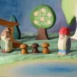 An Ostheimer standing fir tree and Bodo dwarf standing in front of an Ostheimer pond play piece in a small world play scene. There are wooden toy scenery pieces in the background including a apple tree and large birch tree. These wooden figures are part of a wide range of expertly hand crafted wooden toys here at Babipur. 
