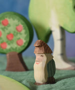 An Ostheimer standing fire tree dwarf wooden toy figure placed in a small world play scene. The dwarf figure has a green coloured outfit with brown hat and a long white beard. The figure has been placed on a green coloured Ostheimer play scarf. This wooden figure is part of a large range of expertly hand crafted, Waldorf inspired, wooden toys here at Babipur. 