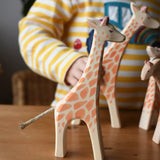 Ostheimer standing giraffe wooden toy figure placed on a wooden surface with other giraffes in the background. 