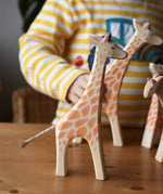 Ostheimer standing giraffe wooden toy figure placed on a wooden surface with other giraffes in the background. 