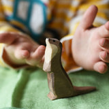 Ostheimer standing sea otter placed on a green cotton play cloth with a child's hand hovering each side of the figure.
