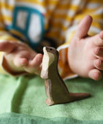 Ostheimer standing sea otter placed on a green cotton play cloth with a child's hand hovering each side of the figure.