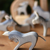 An Ostheimer stubborn donkey wooden toy figure placed on a wooden surface with other donkey's blurred in the background.  Ostheimer's range of hand crafted, heirloom quality wooden toys are available to buy at Babipur.