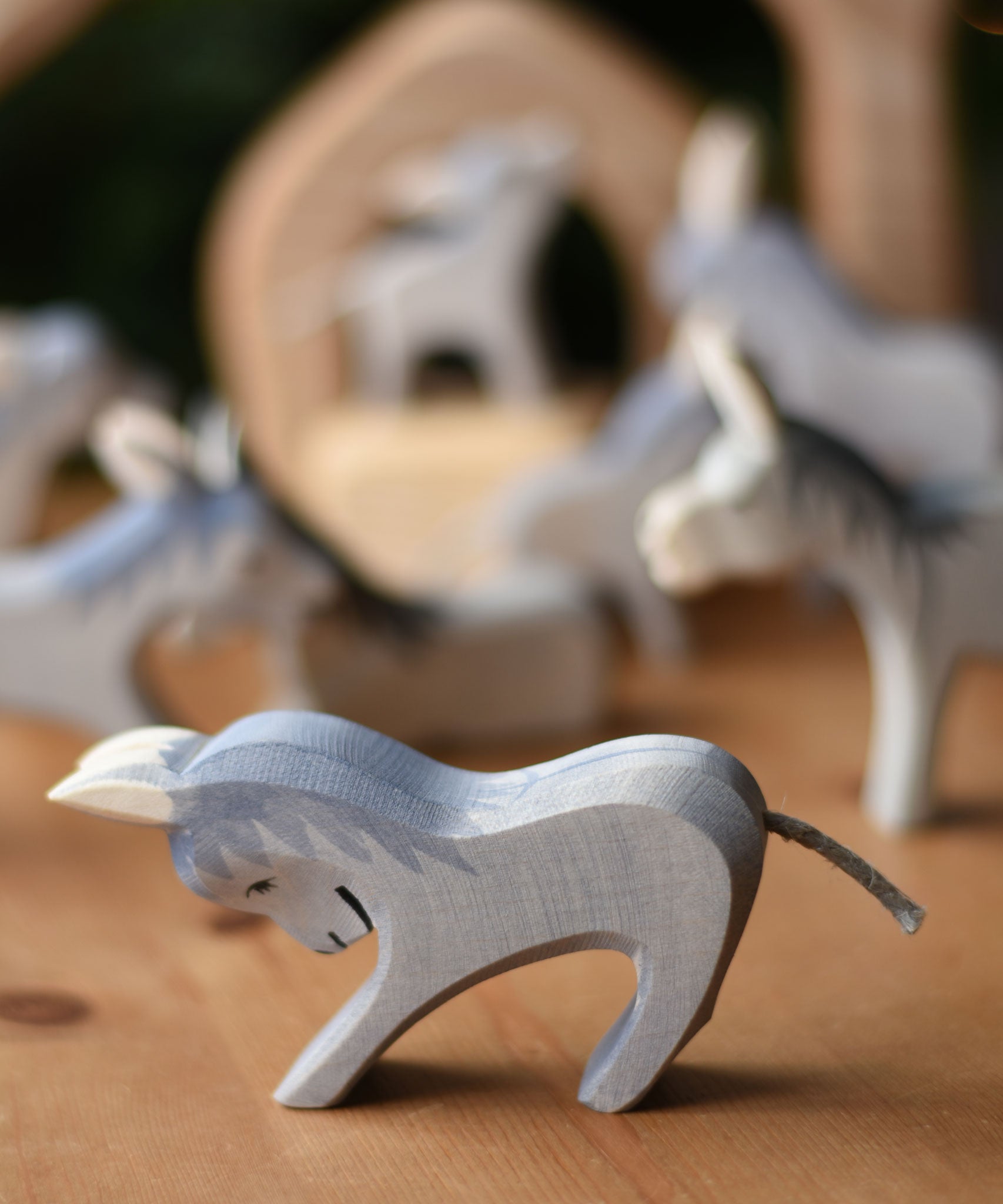 An Ostheimer stubborn donkey wooden toy figure placed on a wooden surface with other donkey's blurred in the background.  Ostheimer's range of hand crafted, heirloom quality wooden toys are available to buy at Babipur.