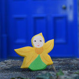 An Ostheimer Sunflower Flower Child placed on a stone wall outdoors in front of a blue door. This wooden figure is part of a large range of expertly hand crafted, Waldorf inspired, wooden toys here at Babipur. 