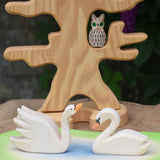Two Ostheimer Swans wooden figures placed on a wooden pond scene piece. One swan has a high neck.