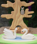 Two Ostheimer Swans wooden figures placed on a wooden pond scene piece. One swan has a high neck.