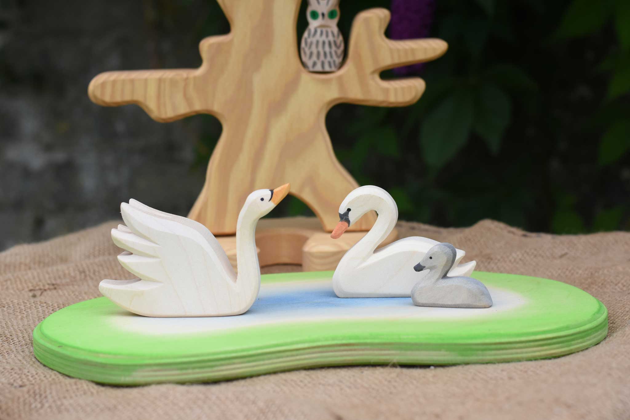 Two Ostheimer swans and a cygnet placed on a pond scene piece in a small world play set up with the bird tree in the background. 