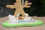 Two Ostheimer swans and a cygnet placed on a pond scene piece in a small world play set up with the bird tree in the background. 