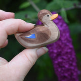 A wooden swimming duck wooden toy figure held in an adult's hand.