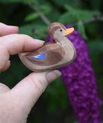 A wooden swimming duck wooden toy figure held in an adult's hand.