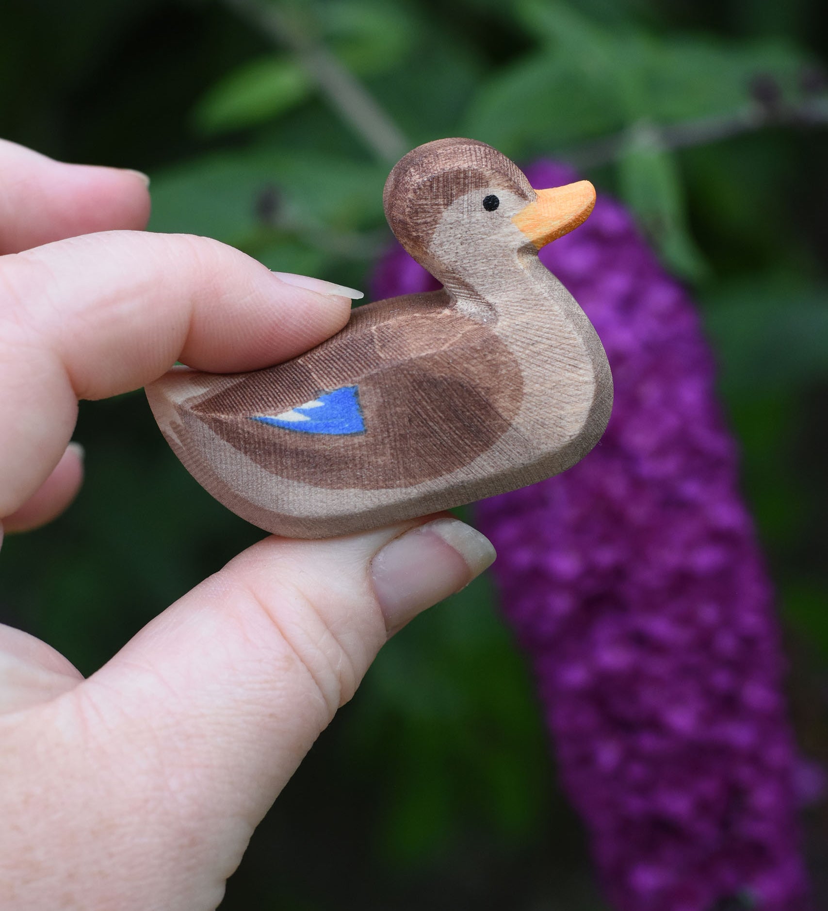A wooden swimming duck wooden toy figure held in an adult's hand.