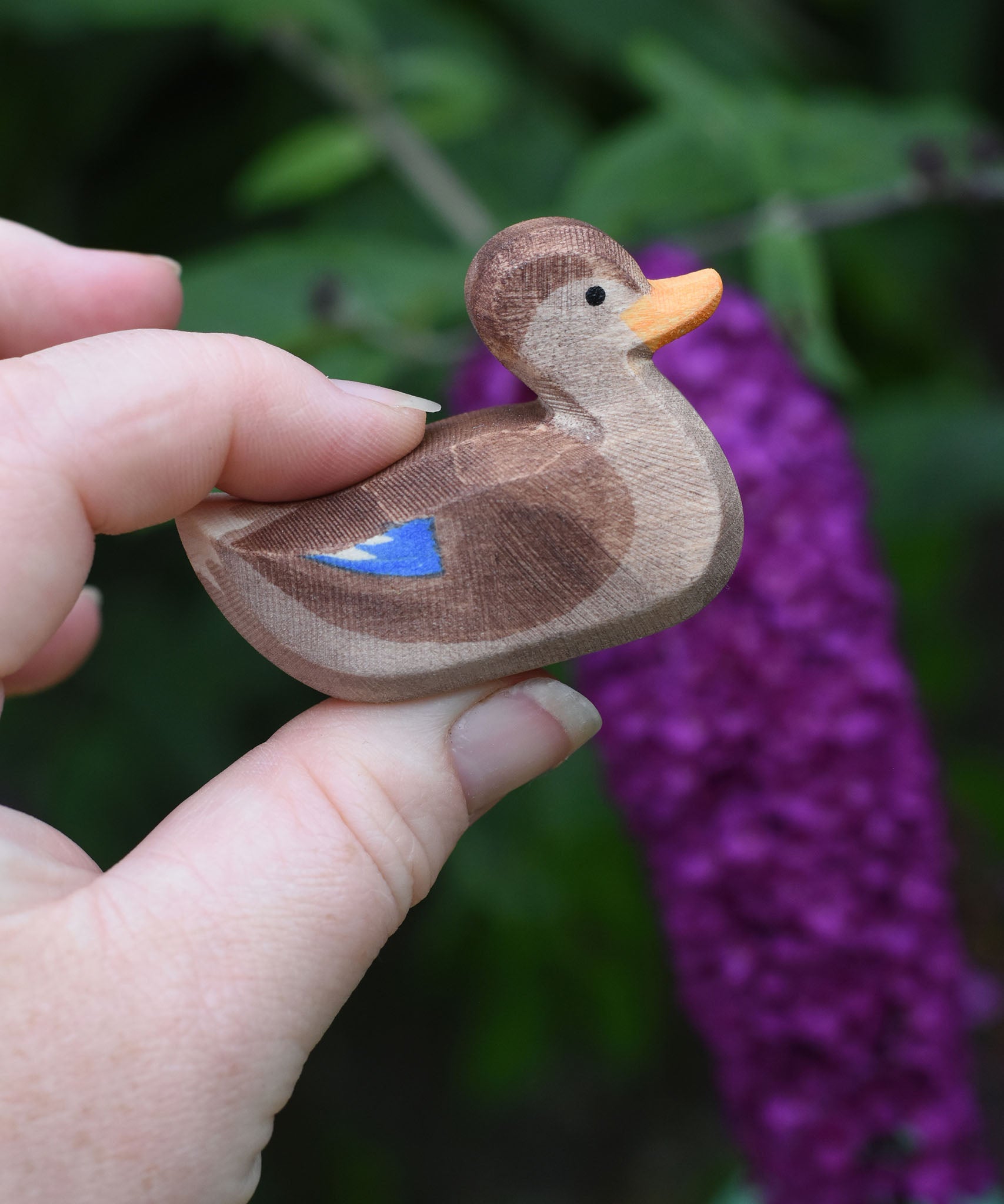 A wooden swimming duck wooden toy figure held in an adult's hand.
