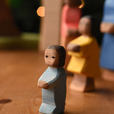 An Ostheimer toddler wooden toy figure with brown skin placed at the front of a small world play scene. These wooden figures are part of a wide range of expertly hand crafted wooden toys here at Babipur.
