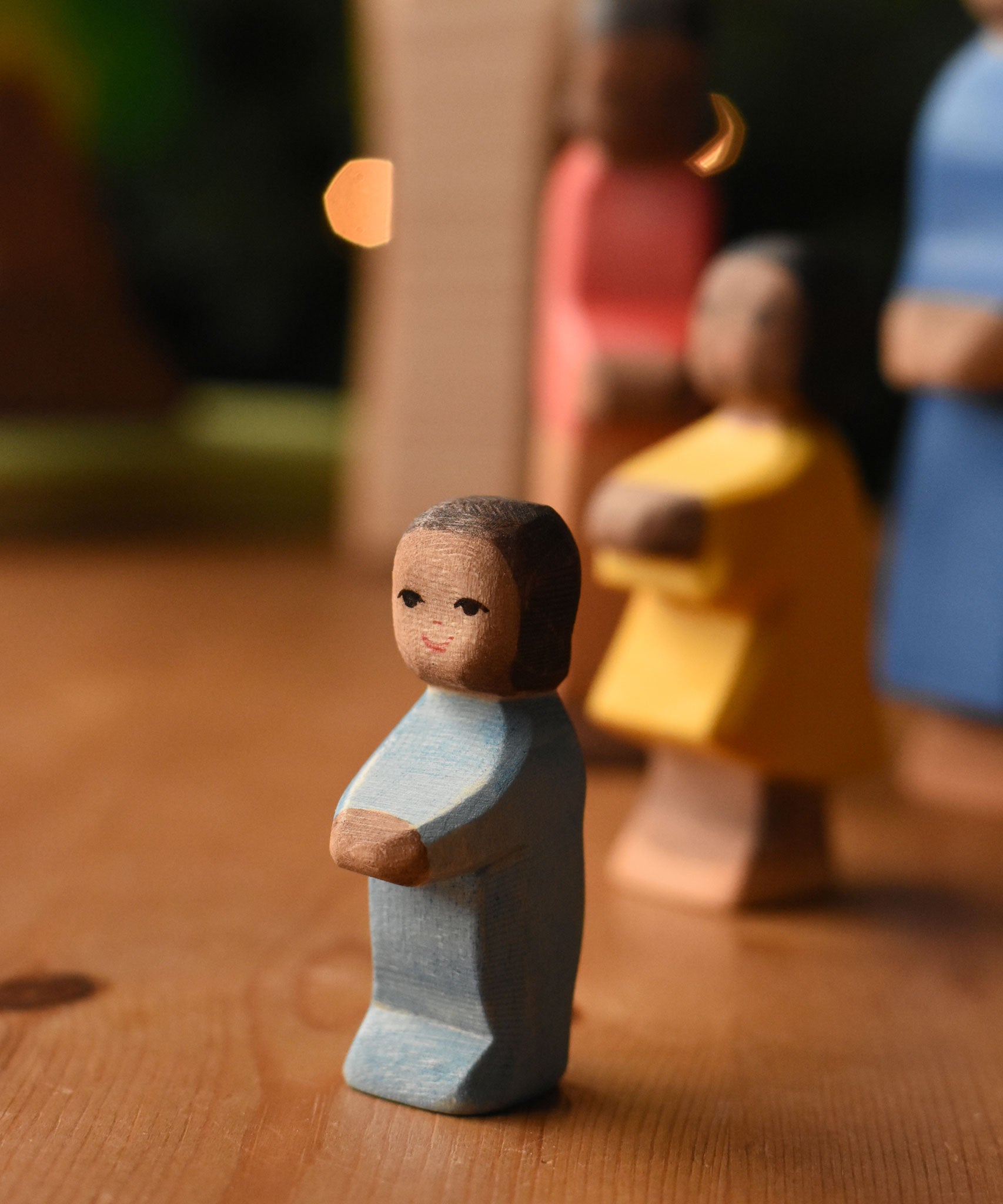 An Ostheimer toddler wooden toy figure with brown skin placed at the front of a small world play scene. These wooden figures are part of a wide range of expertly hand crafted wooden toys here at Babipur.