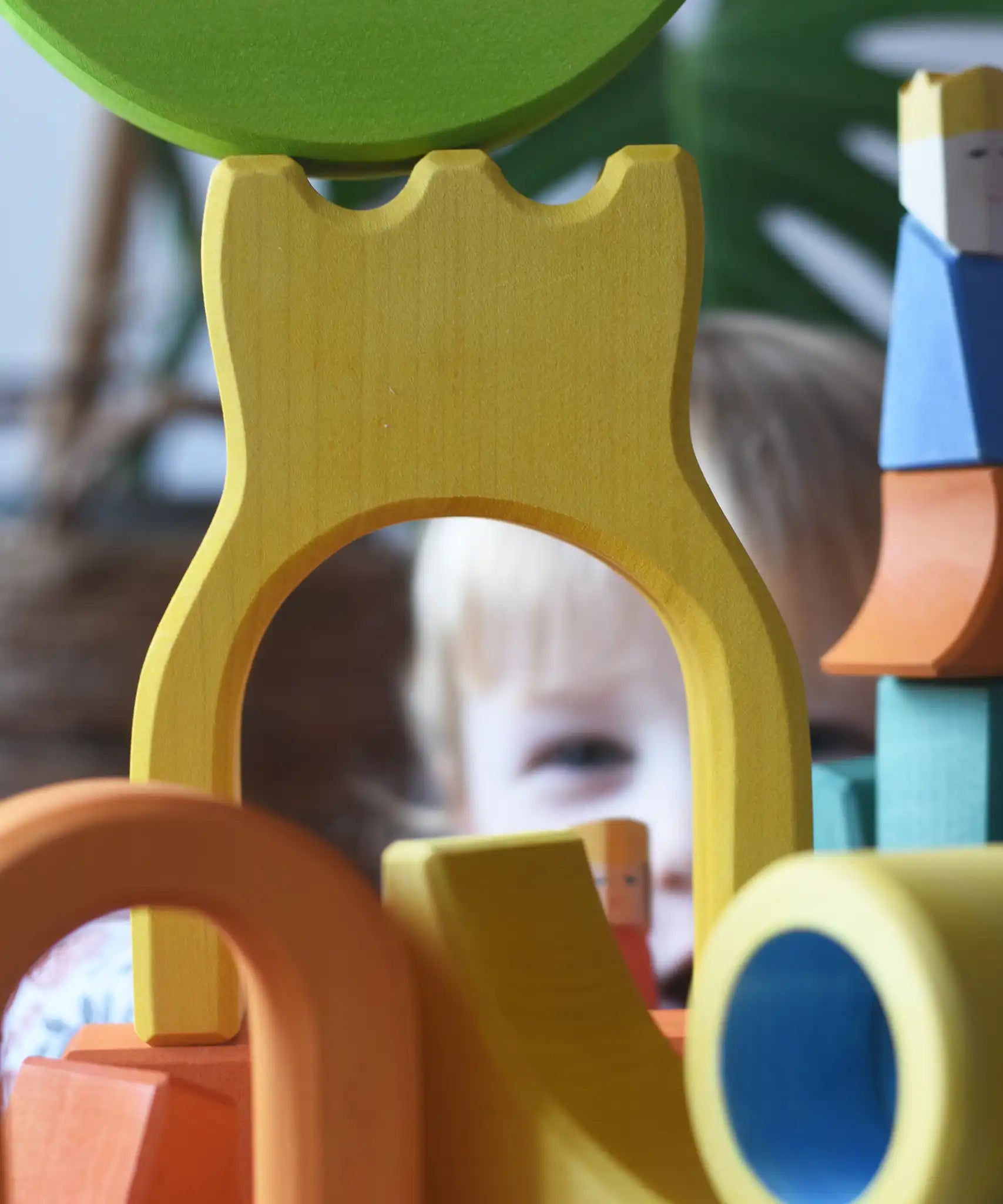 A child peering through the yellow castle shaped piece from the Ostheimer Rainbow Castle Block set. 