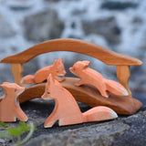 A family of four Ostheimer red fox wooden toy figures. Two fox are placed on w wooden bridge figure with two fox placed on a tone wall in front of the bridge. Check out our full range of expertly crafted wooden toy figures and scenery here at Babipur.