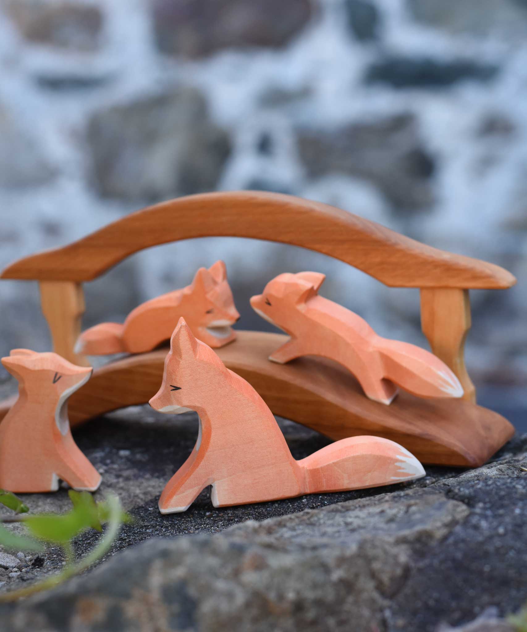 A family of four Ostheimer red fox wooden toy figures. Two fox are placed on w wooden bridge figure with two fox placed on a tone wall in front of the bridge. Check out our full range of expertly crafted wooden toy figures and scenery here at Babipur.