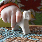Close up of a child's hand holding an Ostheimer white running lamb wooden toy figure.