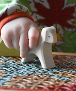 Close up of a child's hand holding an Ostheimer white running lamb wooden toy figure.