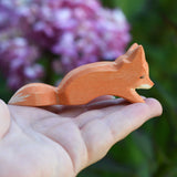 An Ostheimer Small Creeping Fox wooden toy figure shown in an adult's hand for scale. 