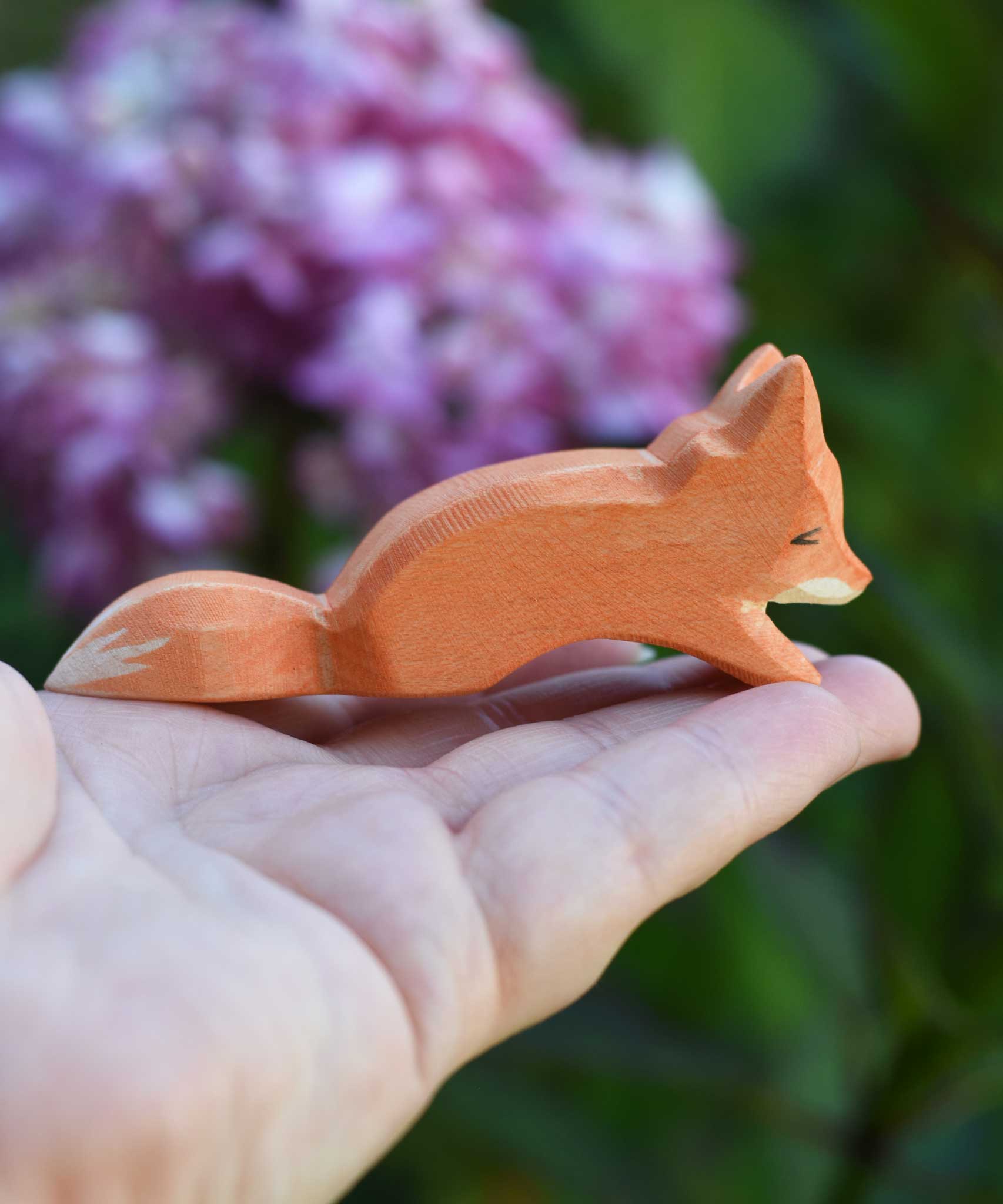 An Ostheimer Small Creeping Fox wooden toy figure shown in an adult's hand for scale. 