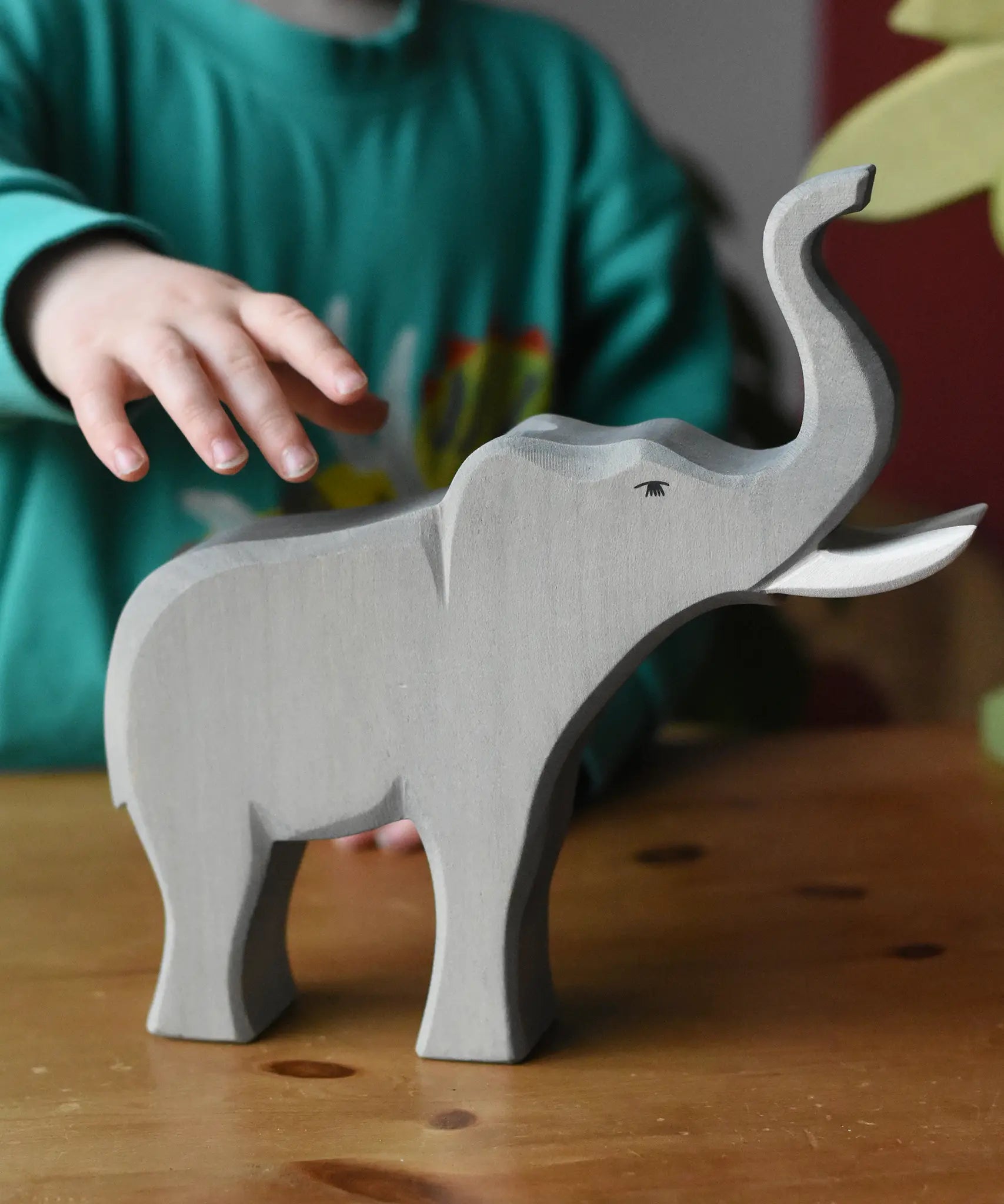 Child's hand reaching for the Ostheimer trumpeting bull elephant wooden toy figure. 