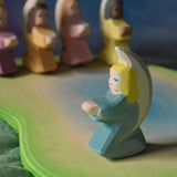 A turquoise blue coloured little angel placed on an Ostheimer pond scene piece. Four other angel can be seen on the other side of the pond piece. These wooden figures are part of a wide range of expertly hand crafted wooden toys here at Babipur. 
