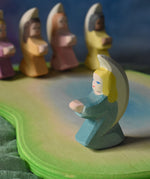 A turquoise blue coloured little angel placed on an Ostheimer pond scene piece. Four other angel can be seen on the other side of the pond piece. These wooden figures are part of a wide range of expertly hand crafted wooden toys here at Babipur. 
