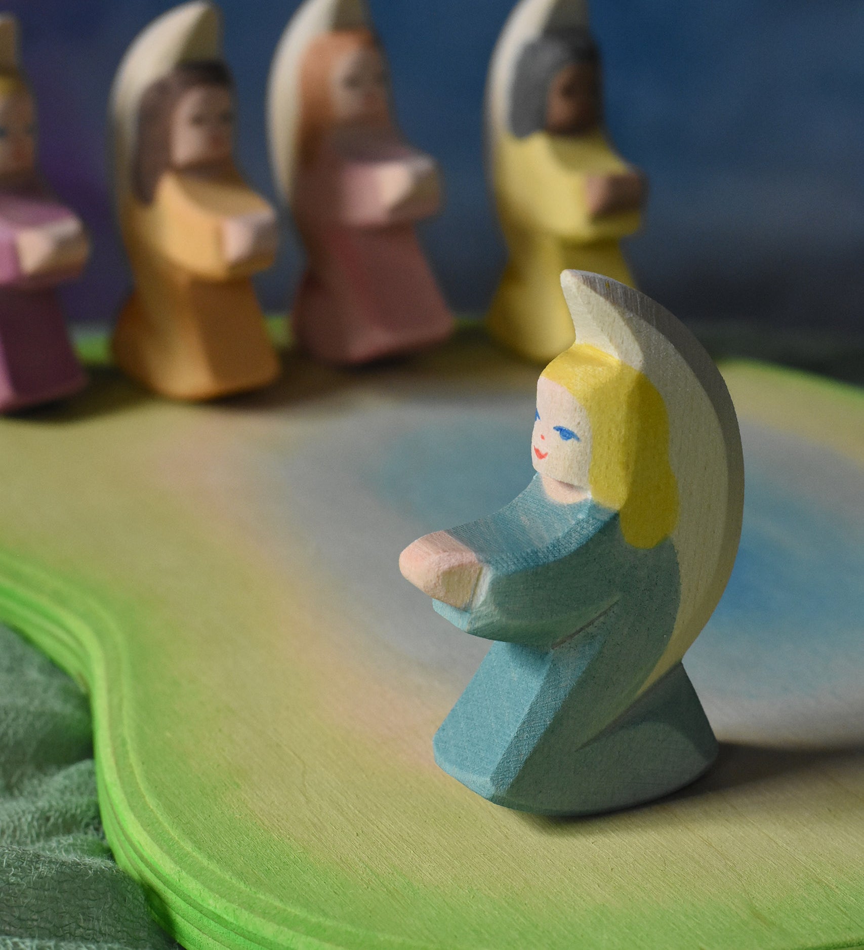 A turquoise blue coloured little angel placed on an Ostheimer pond scene piece. Four other angel can be seen on the other side of the pond piece. These wooden figures are part of a wide range of expertly hand crafted wooden toys here at Babipur. 
