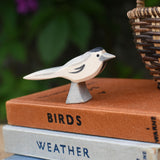 A close up of an Ostheimer wagtail wooden bird figure placed on top of a pile of old books next to a Kraul basket.