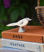 A close up of an Ostheimer wagtail wooden bird figure placed on top of a pile of old books next to a Kraul basket.