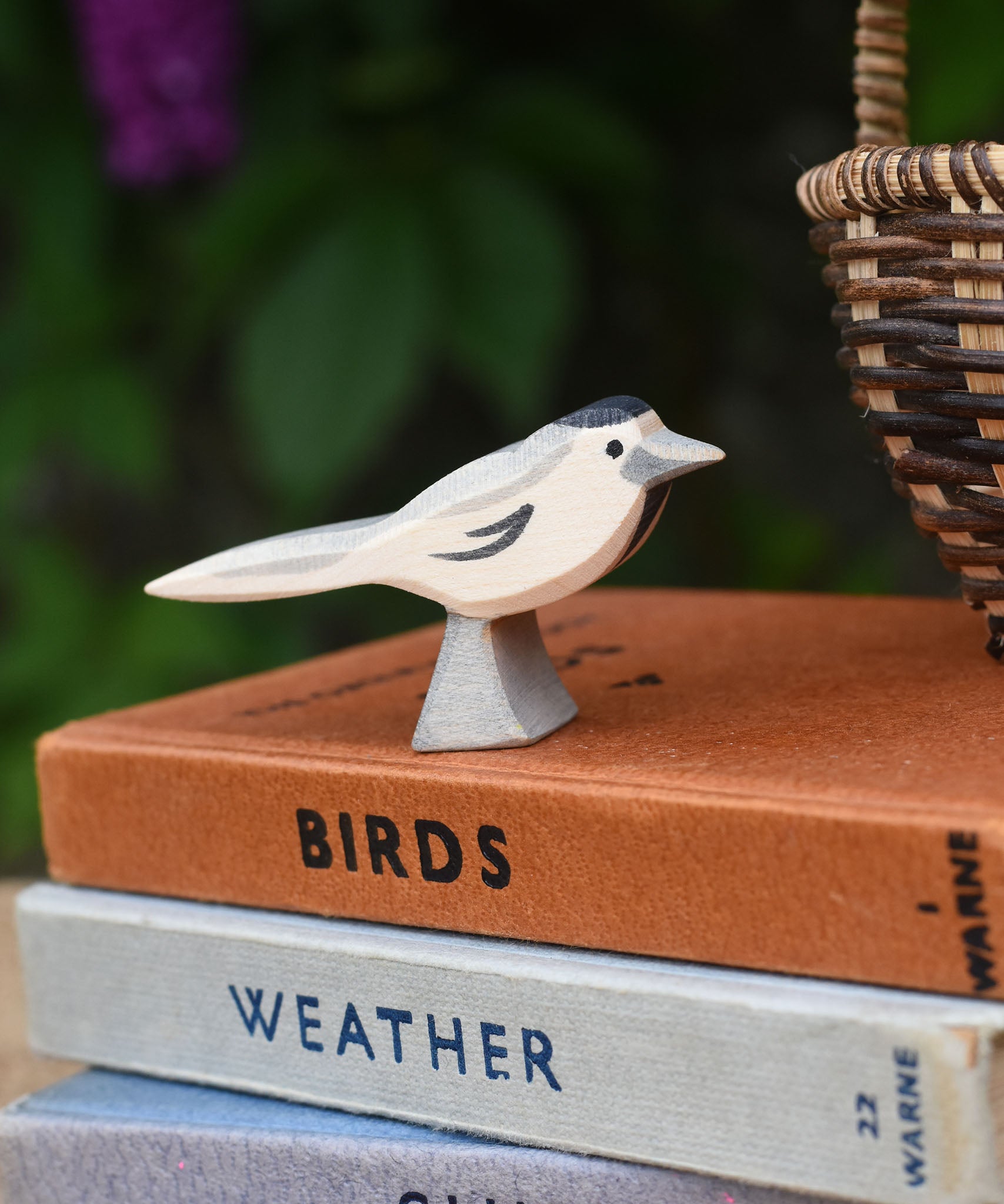 A close up of an Ostheimer wagtail wooden bird figure placed on top of a pile of old books next to a Kraul basket.