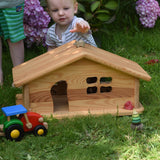 A young child playing outside, the Ostheimer dolls house is in front of them. The child is reaching for a wooden Holztiger mouse that has been placed on the roof. These wooden figures are part of a large range of expertly hand crafted, Waldorf inspired, wooden toys here at Babipur.