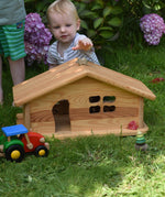 A young child playing outside, the Ostheimer dolls house is in front of them. The child is reaching for a wooden Holztiger mouse that has been placed on the roof. These wooden figures are part of a large range of expertly hand crafted, Waldorf inspired, wooden toys here at Babipur.