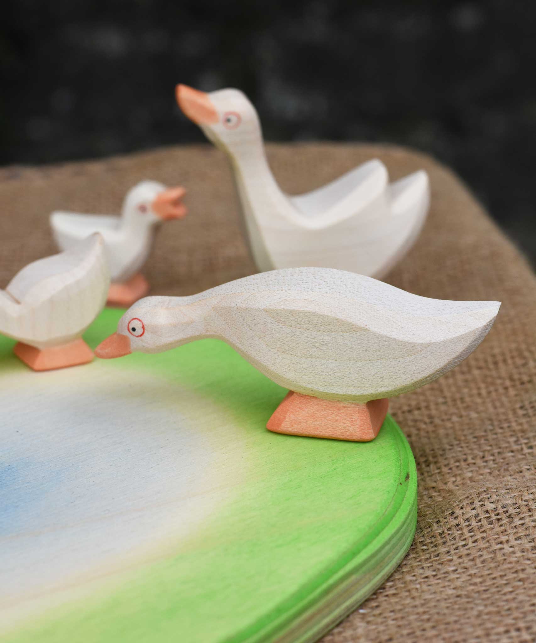 Ostheimer white goose with low neck wooden toy figure placed on an Ostheimer pond scene piece. Other wooden geese figures can be seen in the background. 