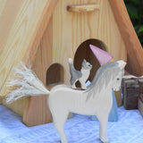 A white Ostheimer white horse with a cat figure placed on his back. An Ostheimer wooden fairy tale dolls house can be seen in the background. These wooden figures are part of a large range of expertly hand crafted, Waldorf inspired, wooden toys here at Babipur. 
