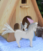 A white Ostheimer white horse with a cat figure placed on his back. An Ostheimer wooden fairy tale dolls house can be seen in the background. These wooden figures are part of a large range of expertly hand crafted, Waldorf inspired, wooden toys here at Babipur. 