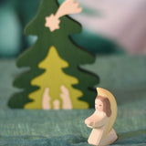 An Ostheimer little angel figure with white outfit placed at the front of small world play scene. There is a Bumbu nativity scene tree in the background. These wooden figures are part of a wide range of expertly hand crafted wooden toys here at Babipur.