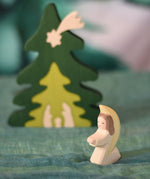 An Ostheimer little angel figure with white outfit placed at the front of small world play scene. There is a Bumbu nativity scene tree in the background. These wooden figures are part of a wide range of expertly hand crafted wooden toys here at Babipur.